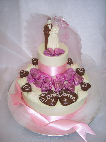 a picture of a chocolate bride and groom decorated with initialed love hearts on a chocolate tier